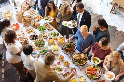 A diverse group of people enjoying a buffet with various dishes. The buffet features salads, meats, and desserts. Guests serve themselves from the buffet table. Friends at lunch buffet together.