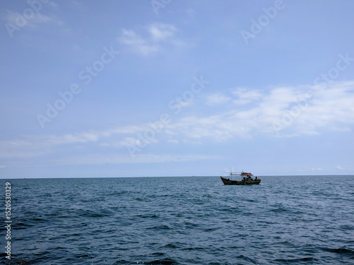 A small fishing boat floats alone on the calm, expansive blue ocean under a clear sky.