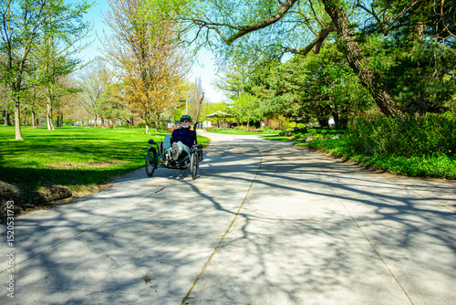 Healthy active outdoor lifestyle: senior man hat sunglasses beard cycling on a recumbant tricycle on a path in sunshine on the Toronto Islands shot in spring room for text