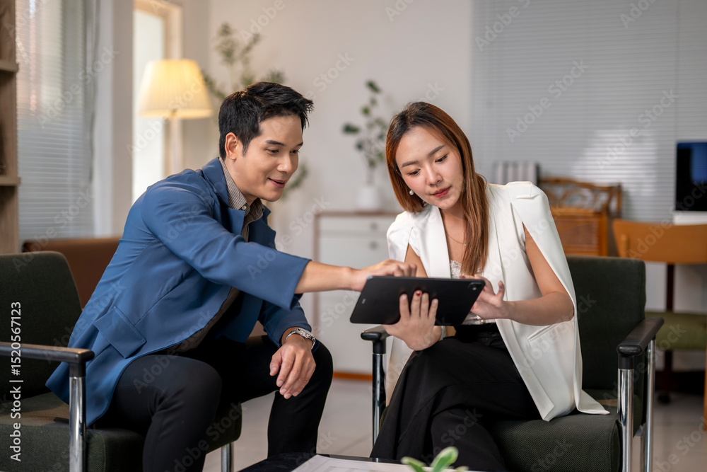 Fototapeta premium A man and a woman are sitting in chairs and looking at a tablet