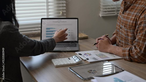 Two people are sitting at a table with a laptop and a calculator. They are working on a project together