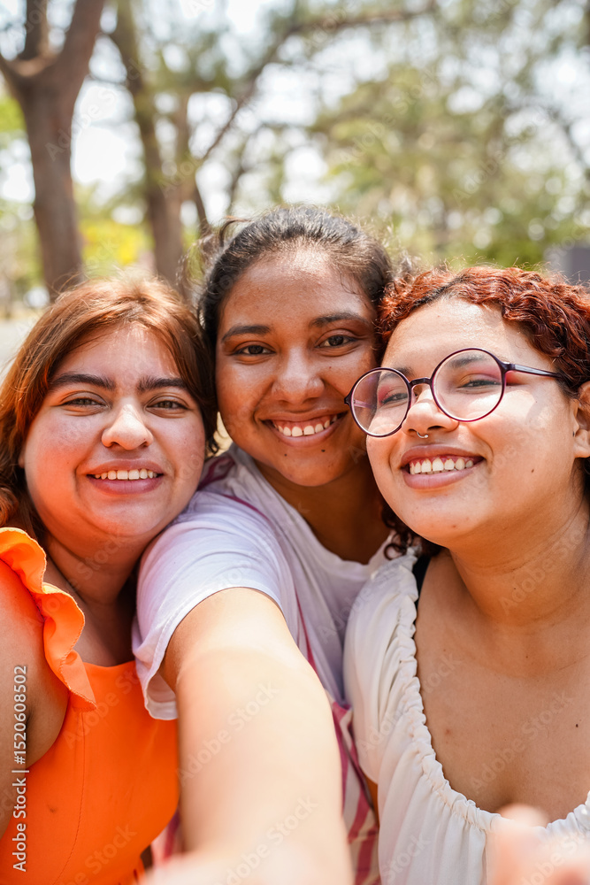Fototapeta premium Three happy latin friends taking a selfie in a park