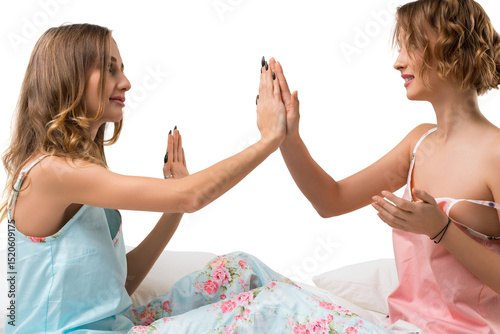 Two friends playing a hand game while lounging on a bed in casual outfits