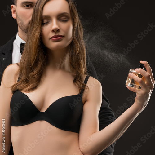 Woman applying perfume with a man standing behind in elegant attire