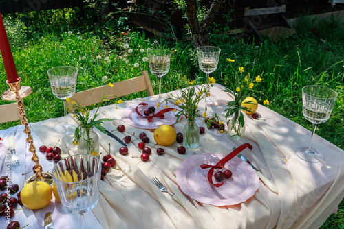 Fototapeta holiday concept - romantic table setting with white tablecloth, plates, crystal glasses, cherries