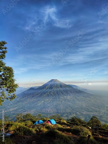 Majestic Mount Sindoro stands tall under a clear blue sky, with wispy clouds and a bright green foreground hinting at a panoramic landscape. Nature of Indonesia. photo