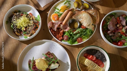 table filled with various breakfast plates, including omelets, pancakes, toast, fruits, croissants, cereals. Bright natural light, summer morning atmosphere in cozy cafe or restaurant.
