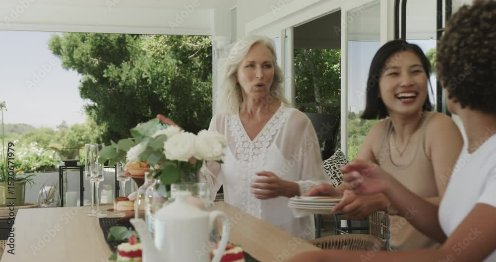 Diverse friends opening glass doors, carrying roses and treats onto patio table, waving and hugging