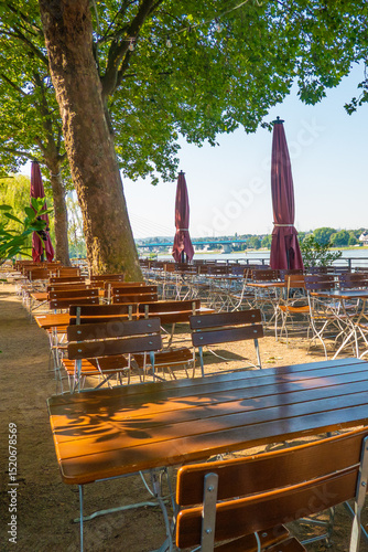 Outdoor tables and chairs in a beer garden close to the river Rhine in Neuwied, Germany, under shade trees on sunny day