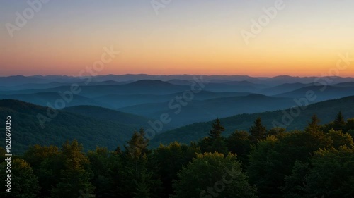 Mountain range vista at sunset. Gradient sky above layers of hills covered in trees