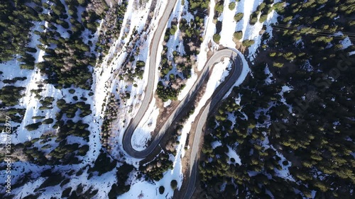 Top-down aerial rotates slowly above snowy switchback road in Maloja Pass, Switzerland