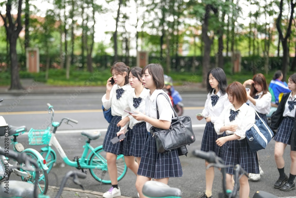 Fototapeta premium In early June in Pudong, Shanghai, seven Japanese high school girls in summer uniforms walk together down a city street, smiling and chatting as they head to school under the soft morning sunlight.