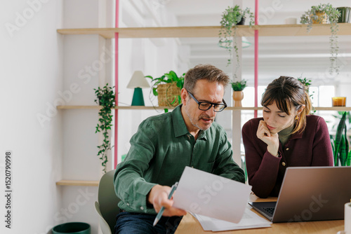 Two colleagues collaborating in a modern office with a laptop and paperwork