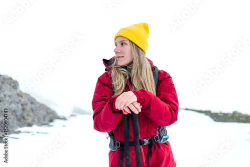 Woman in red jacket and yellow hat hiking in snowy mountain landscape