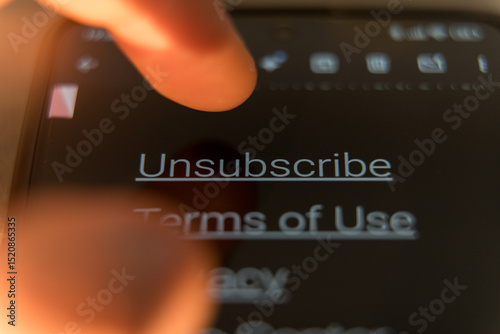 Close-up of a finger to tap the Unsubscribe link on a smartphone screen in dark mode
