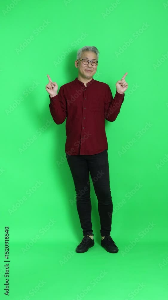 The senior East Asian man in smart casual clothes is standing against a chroma key green background.