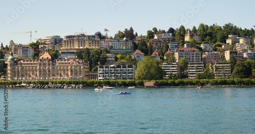 Wallpaper Mural 30-05-2025 Lucerne, Switzerland. Tourist Ferryboat sailing close to shore, past Mandarin Oriental Palace Hotel. Riverside promenade with tourists enjoying a sunny summer day, real time footage Torontodigital.ca