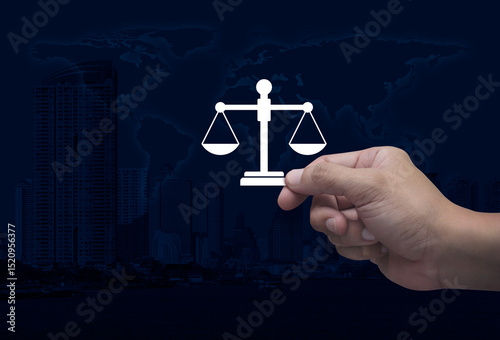 Fototapeta Naklejka Na Ścianę i Meble -  Hand holding law flat icon in fingers over world map, modern city tower and skyscraper, Business legal service concept, Elements of this image furnished by NASA