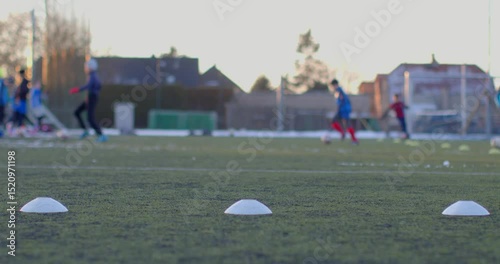 Dedicated soccer players are practicing drills on a large field filled with training cones