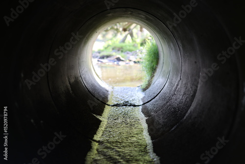 View through a round concrete tunnel carrying a stream beneath a road