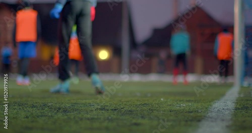 In the evening, players are engaged in practice on a soccer field with houses visible in the background
