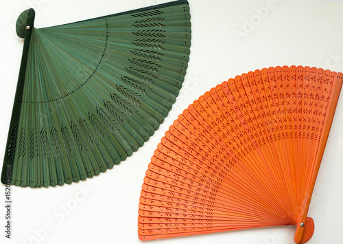 Colorful traditional Japanese hand fans in green and orange displayed on a white wall, showcasing intricate patterns. Bright summer decor concept.