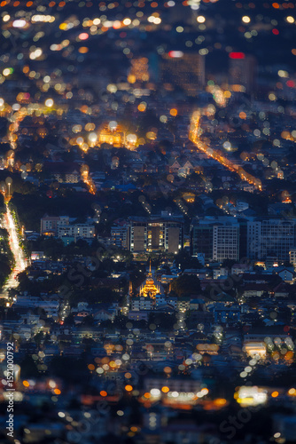golden chedi of wat suan dok gleams under the soft evening sky, with dreamy bokeh foreground lights captured from doi suthep scenic viewpoint in chiang mai.