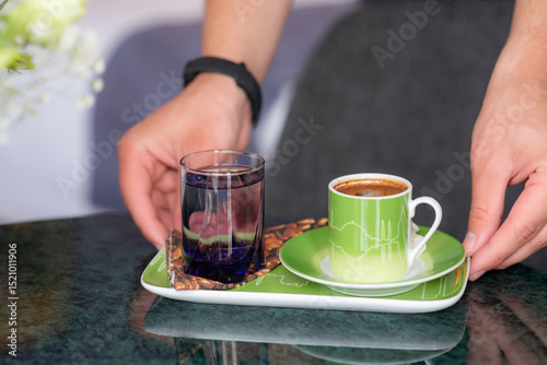 Hands serving a welcome gesture at a hotel, Turkish coffee with Turkish delight sweets and water on a marble tabletop in a hotel room setting with soft window light