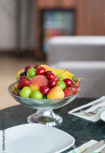 Colorful fresh fruit bowl on hotel room counter with armchair, bed and lampshade showing in the background