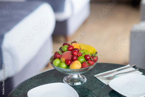 Colorful fresh fruit bowl on hotel room counter with armchair, bed and lampshade showing in the background