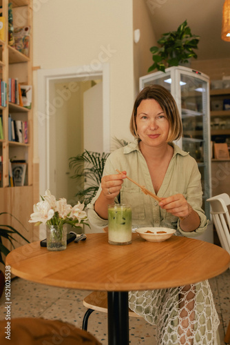 Middle-aged woman scrolls her social media feed on mobile phone in a cozy cafe. Small business. Using phone for business, online shopping, transfer money, financial, internet banking