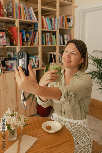 Middle-aged woman scrolls her social media feed on mobile phone in a cozy cafe. Small business. Using phone for business, online shopping, transfer money, financial, internet banking