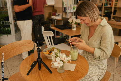 Middle-aged woman is video blogging in a cafe on a phone with a tripod. Small business. Using phone for business, online shopping, transfer money, financial, internet banking. Part of a series
