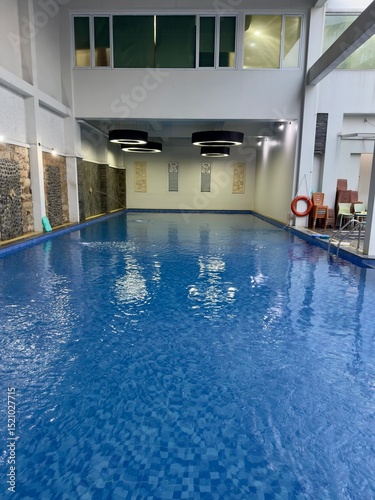 An inviting indoor swimming pool stretches out under a high ceiling, with clear, still water reflecting soft lighting