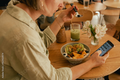 Middle-aged woman scrolls her social media feed on mobile phone in a cozy cafe. Small business. Using phone for business, online shopping, transfer money, financial, internet banking