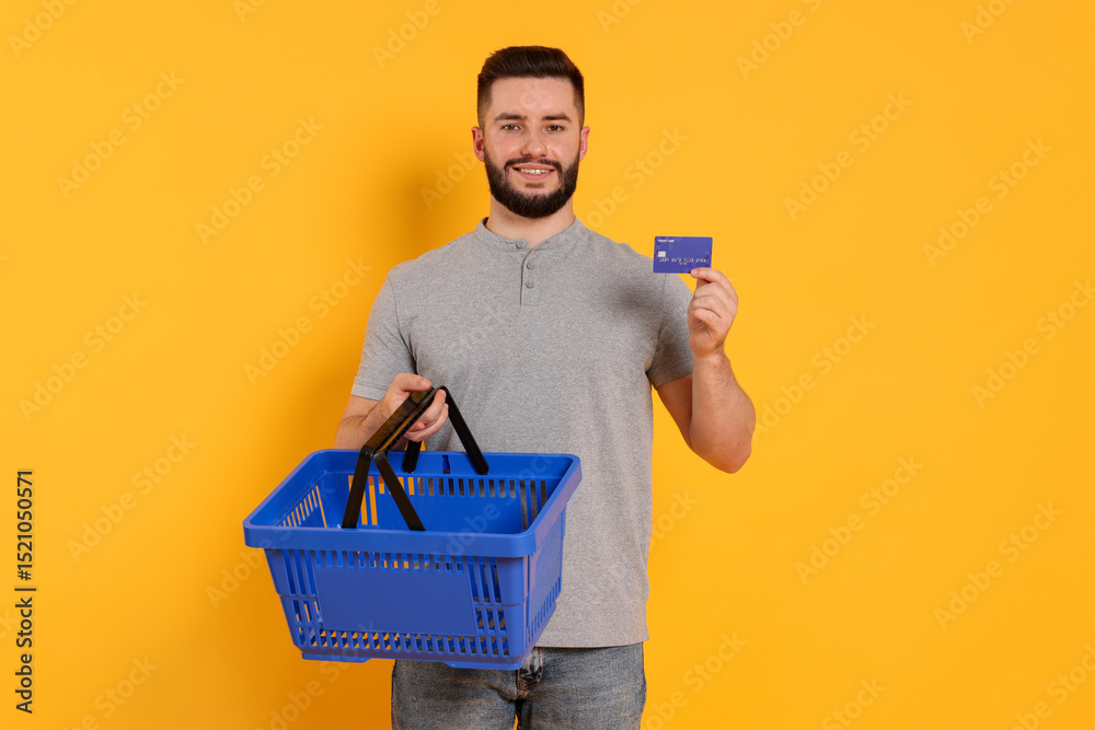 Fototapeta premium Man with empty shopping basket and credit card on orange background