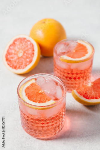 A refreshing negroni rosa cocktail served in a textured glass with ice, garnished with a slice of pink grapefruit, set against a light background. Summer party drink recipe, beverages menu.