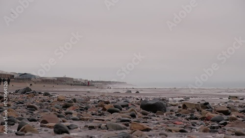 EDINBURGH, SCOTLAND, UK - JANUARY 5, 2024: Calm, cloudy sunrise at Portobello Beach, where the rocky shore meets the gentle waves of the sea, people walking on the beach.