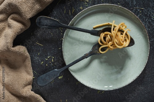 Still life - pasta in a plate and a fork with a spoon on the table. Food on a dark background