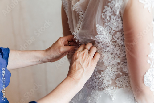 Close-up of the bride's mother's hands fastening the buttons on her dress