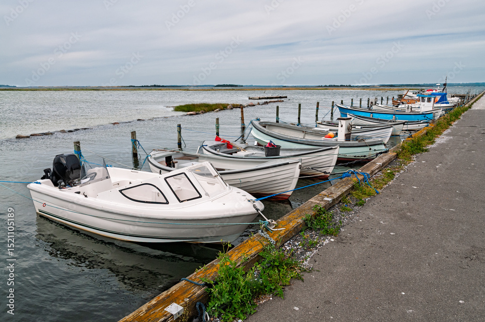 Fototapeta premium Several small boats are secured at a dock along a peaceful waterway, surrounded by flat waters and gentle clouds above.
