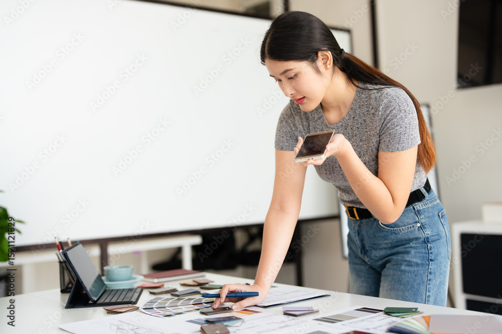 Fototapeta premium Interior designer talking on cellphone with client, discussing new project, In studio office with blueprint drawing color swatches and material, design develop, Copy Space