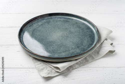 An empty grey textured plate with a napkin on a white wooden table