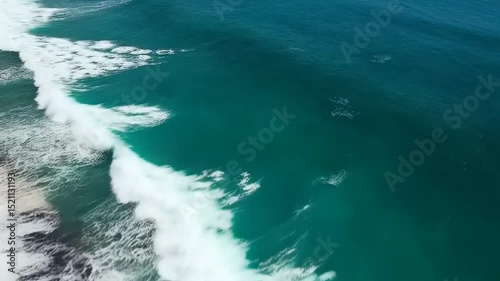 Aerial view of turquoise ocean waves crashing onto a black sand beach under a clear sky