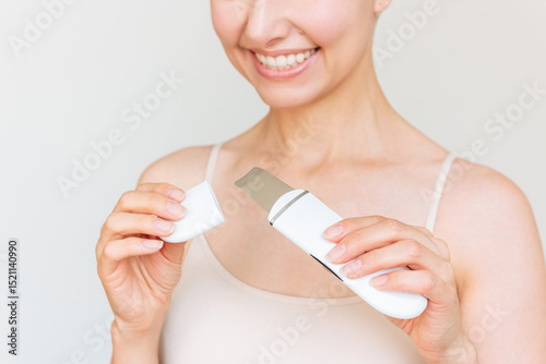 Young Beautiful Caucasian brunette woman in white clothes using a white ultrasonic facial cleaning device. Skin care. 