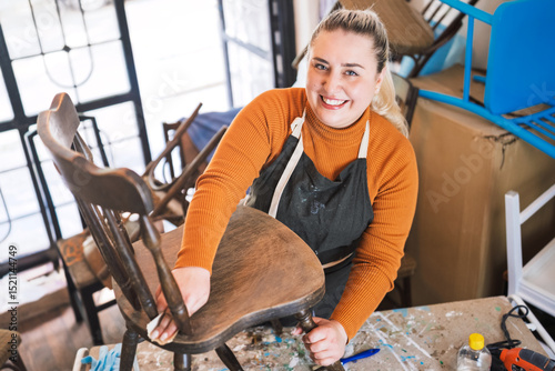 joyful woman restoring antique wooden chair in home workshop