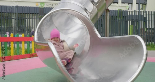 A cheerful preschool child slides down a metal slide on a children's playground, experiencing pure joy and excitement while playing outdoors. Child enjoying slide ride on playground.