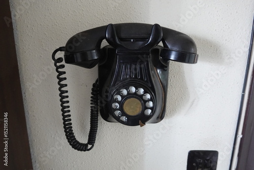 Black rotary phone hanging on white wall