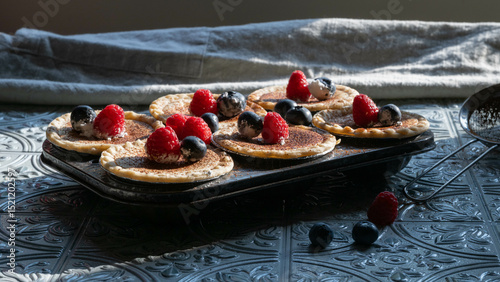Cream cheese tartlets or mini pies with cacao espresso powder sprinkles and fresh raspberries and blueberries.
