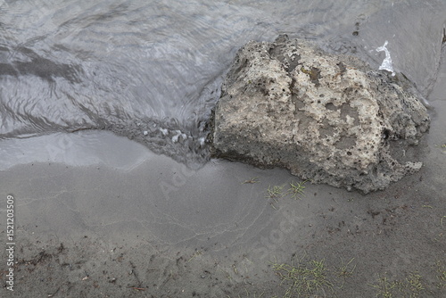 Fototapeta Naklejka Na Ścianę i Meble -  a porous pumice stone on black sand with slow flowing water rippling around it